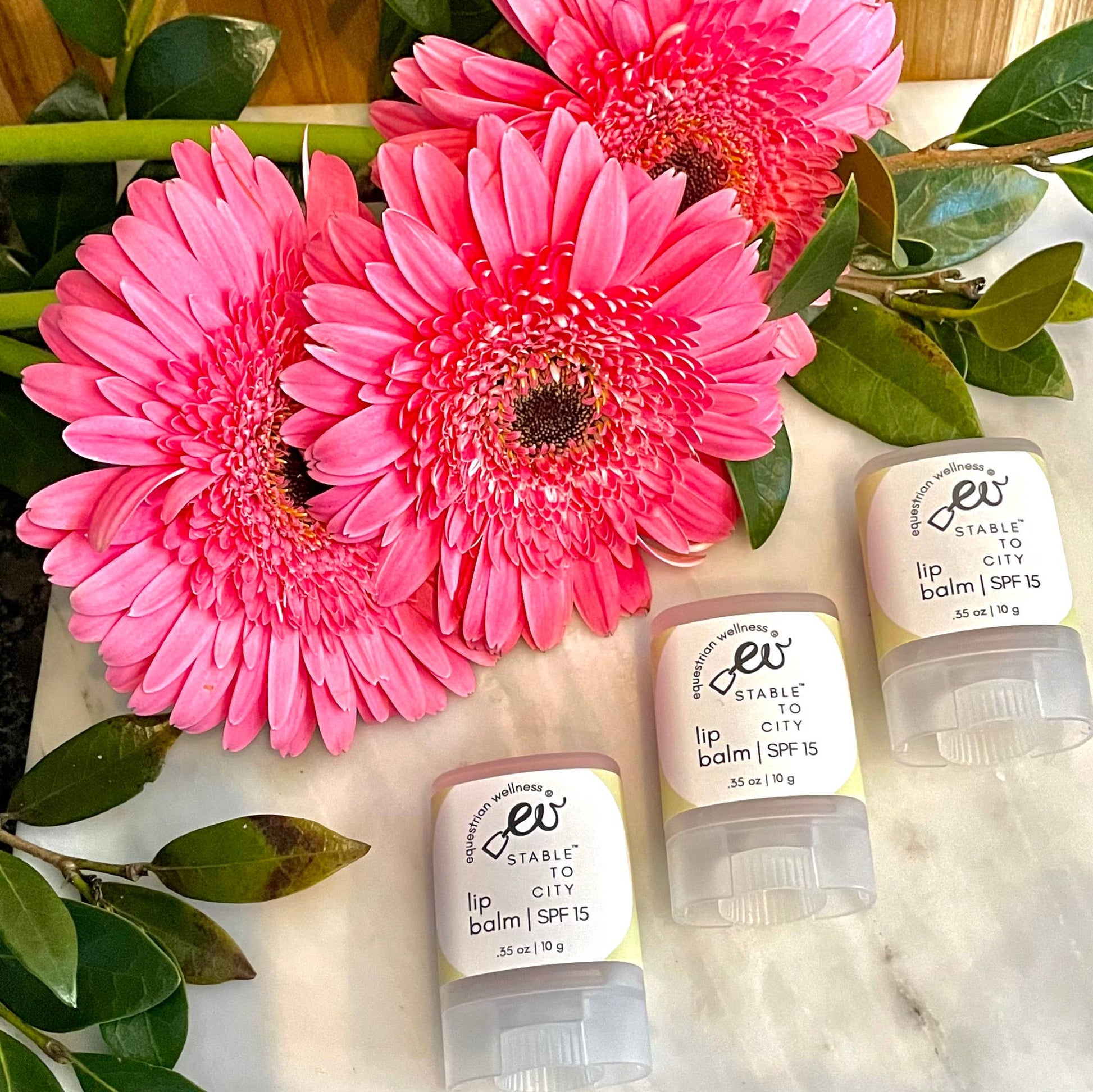 three sticks of organic lip balm on a marble coutnertop with a boquet of flowers