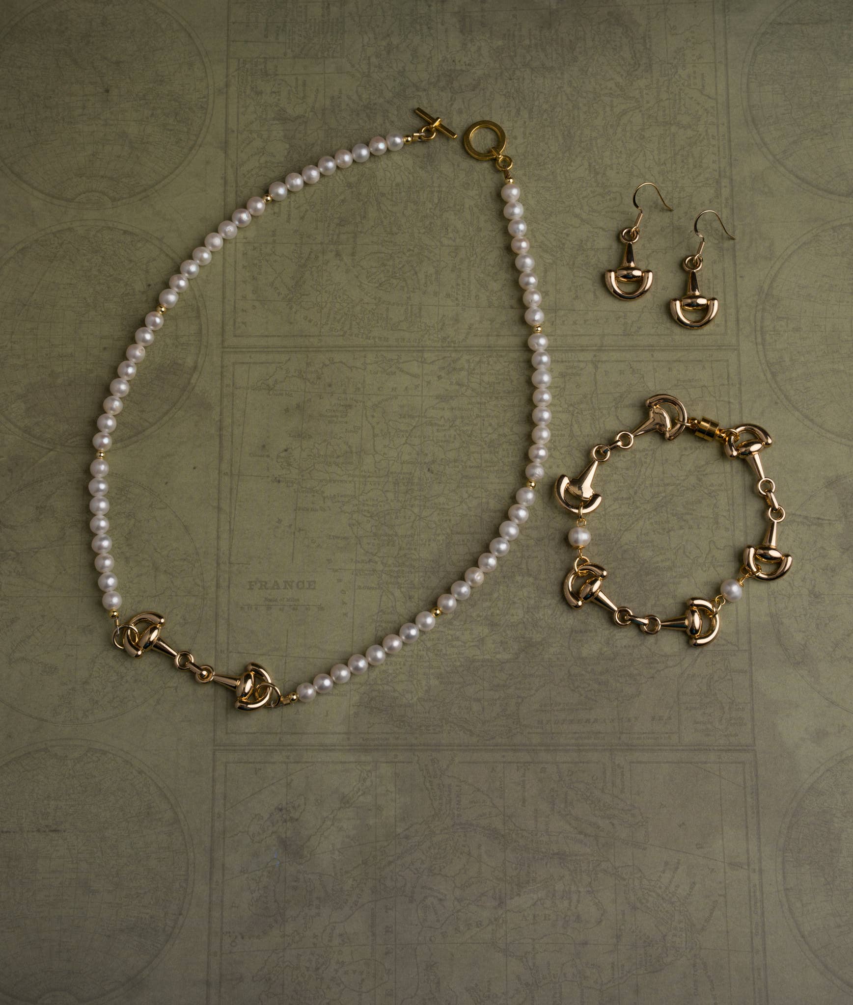 Pearl equestrian necklace with gold clasp, bracelet, and earrings on a textured surface