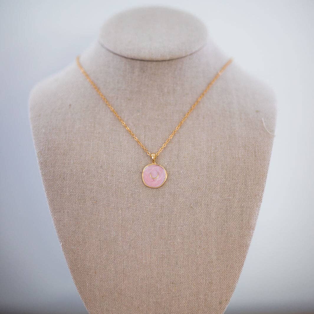 Gold necklace with a pink pendant on a mannequin bust against a plain background