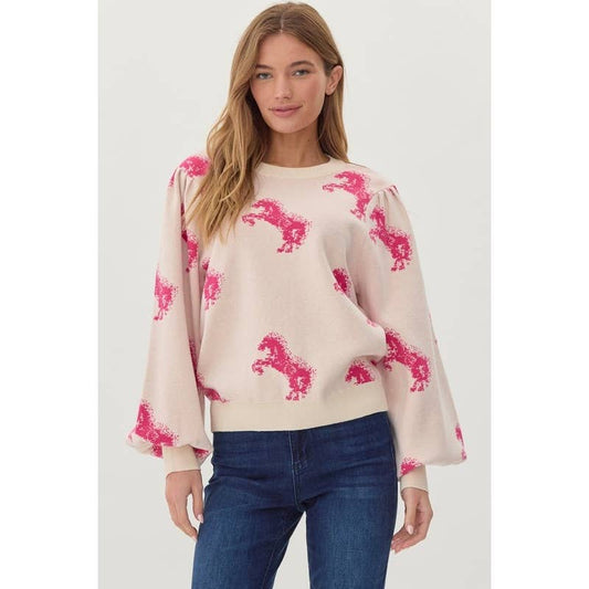 A woman wearing a beige knit sweater top with a horse pattern and long sleeves, paired with blue jeans.