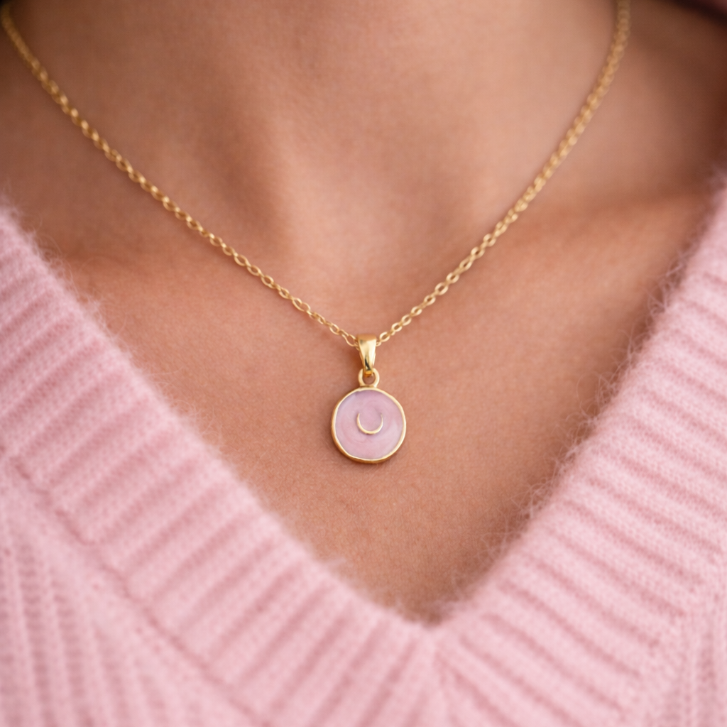 Gold horse shoe necklace with a pink pendant worn by a person in a pink sweater.