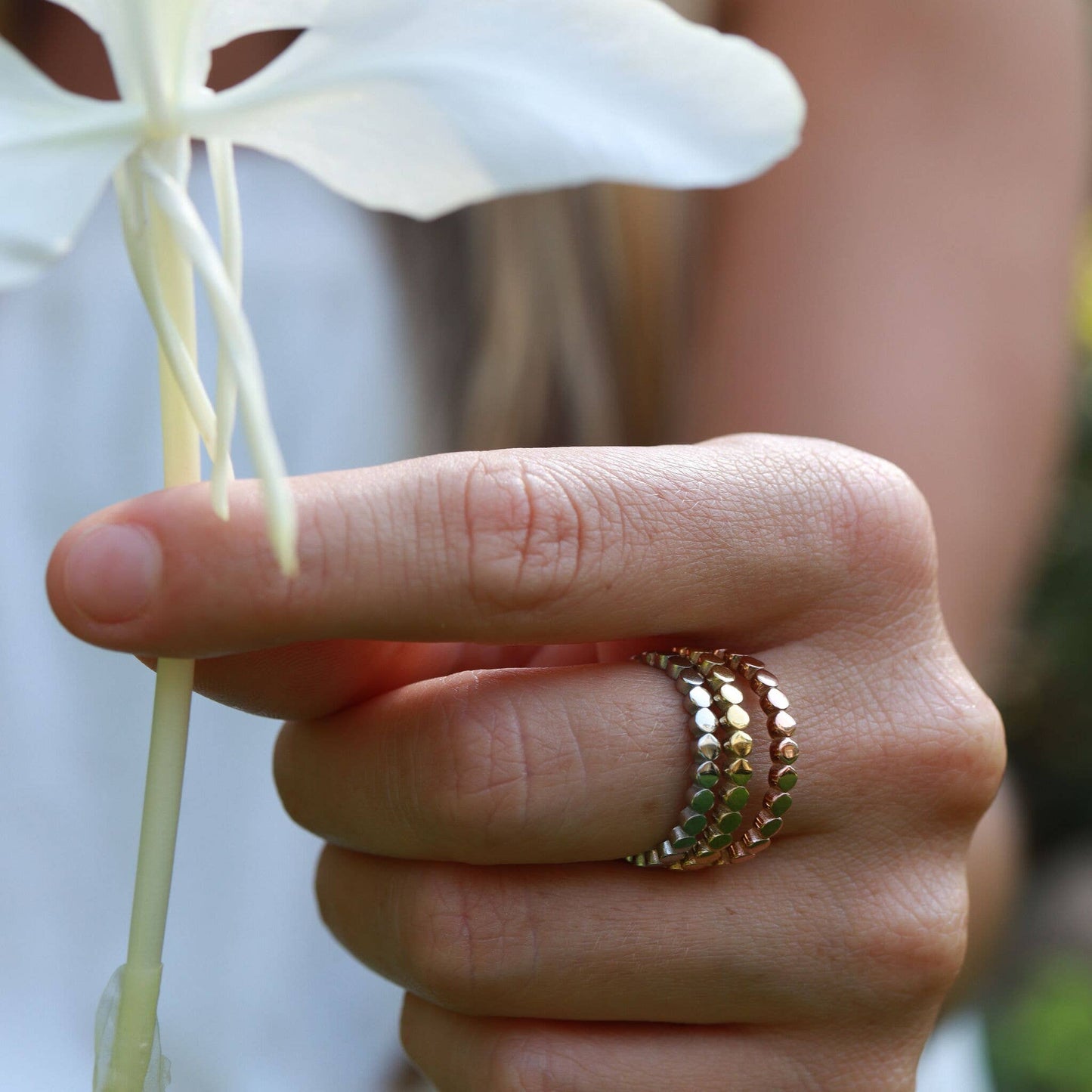 Hand holding a white flower with two rings on a blurred background