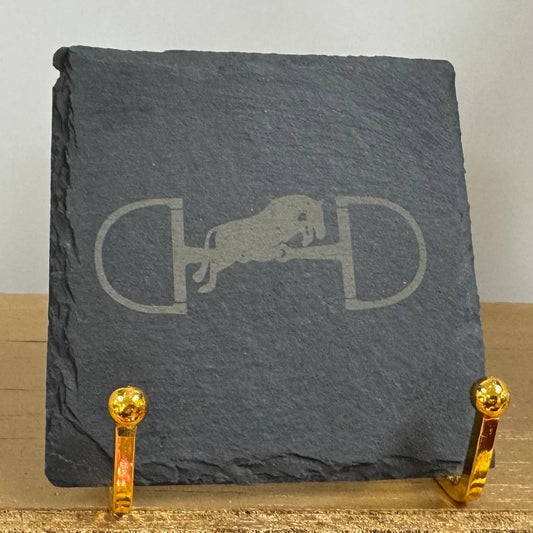 A slate coaster with an engraved jumping horse and bit design, displayed on a stand.