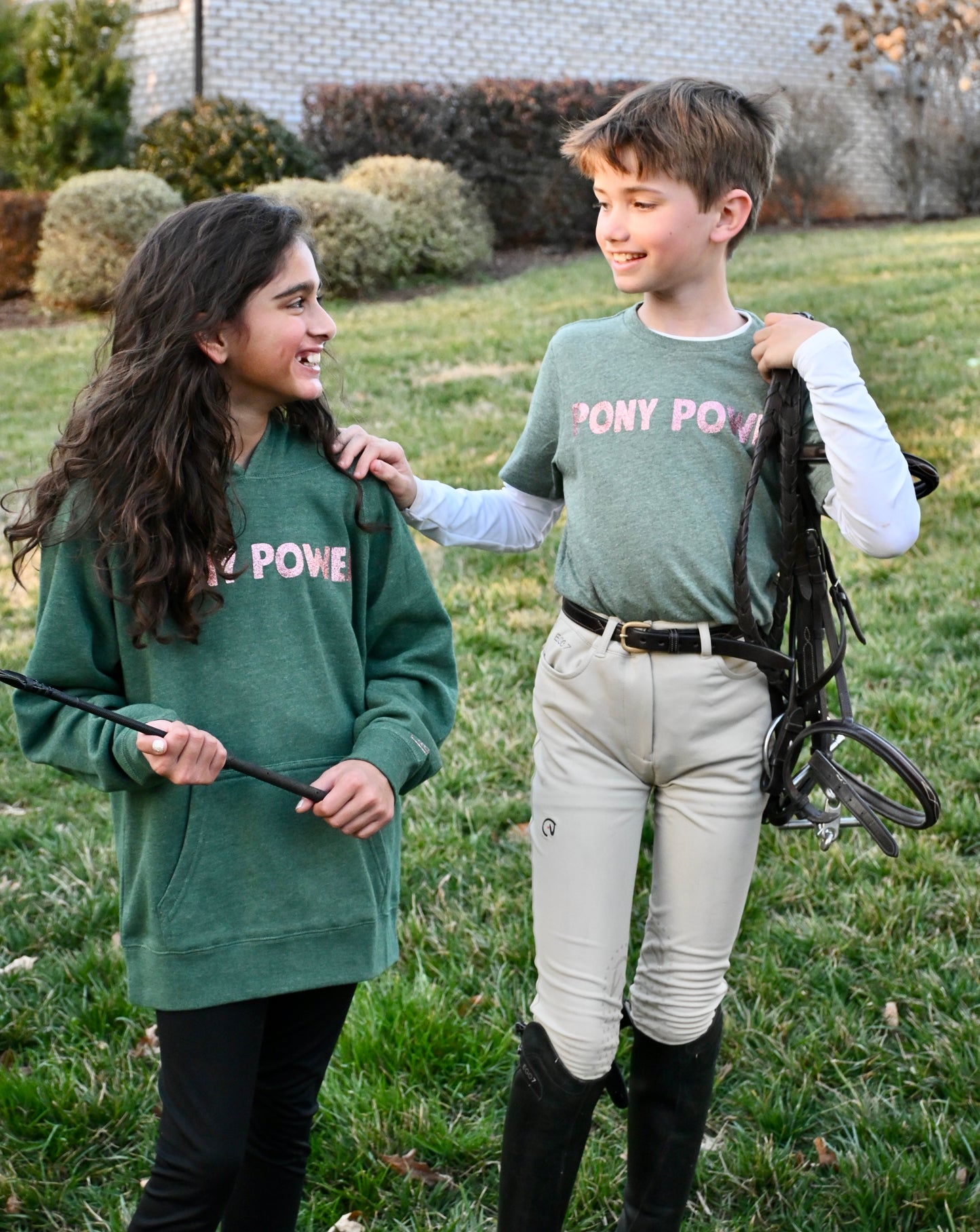 Two children, a boy and a girl, wearing green bamboo shirts with 'Pony Power' text on them, standing outdoors.