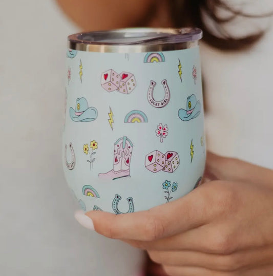 A stainless wine tumbler with a colorful pattern, including what appears to be a unicorn, hearts, and other playful designs, being held by a person.