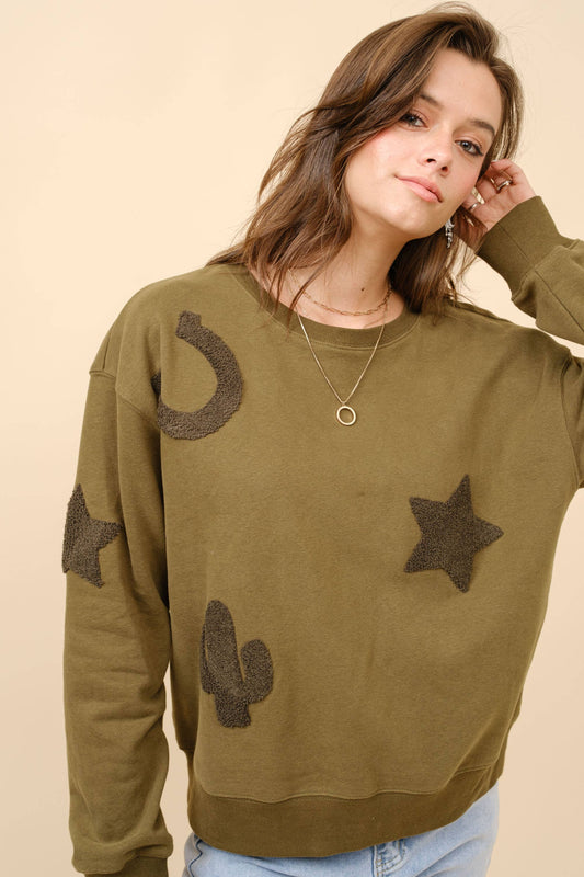 A woman wearing a green textured patchwork sweatshirt with star and cactus designs.