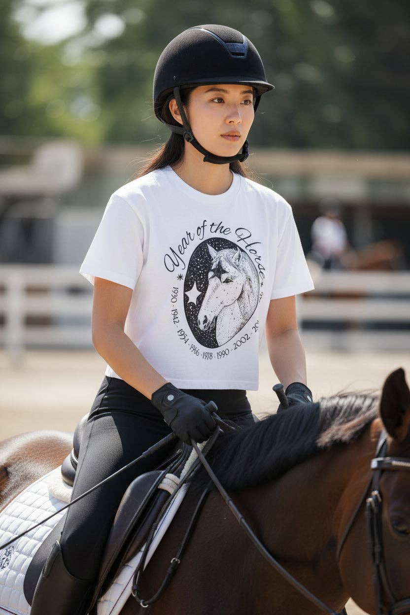 Person riding a horse wearing a helmet and a white t-shirt with a horse graphic.