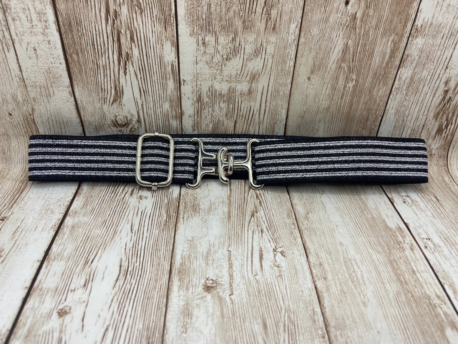 Black and gray striped belt with gold buckle on a wooden surface